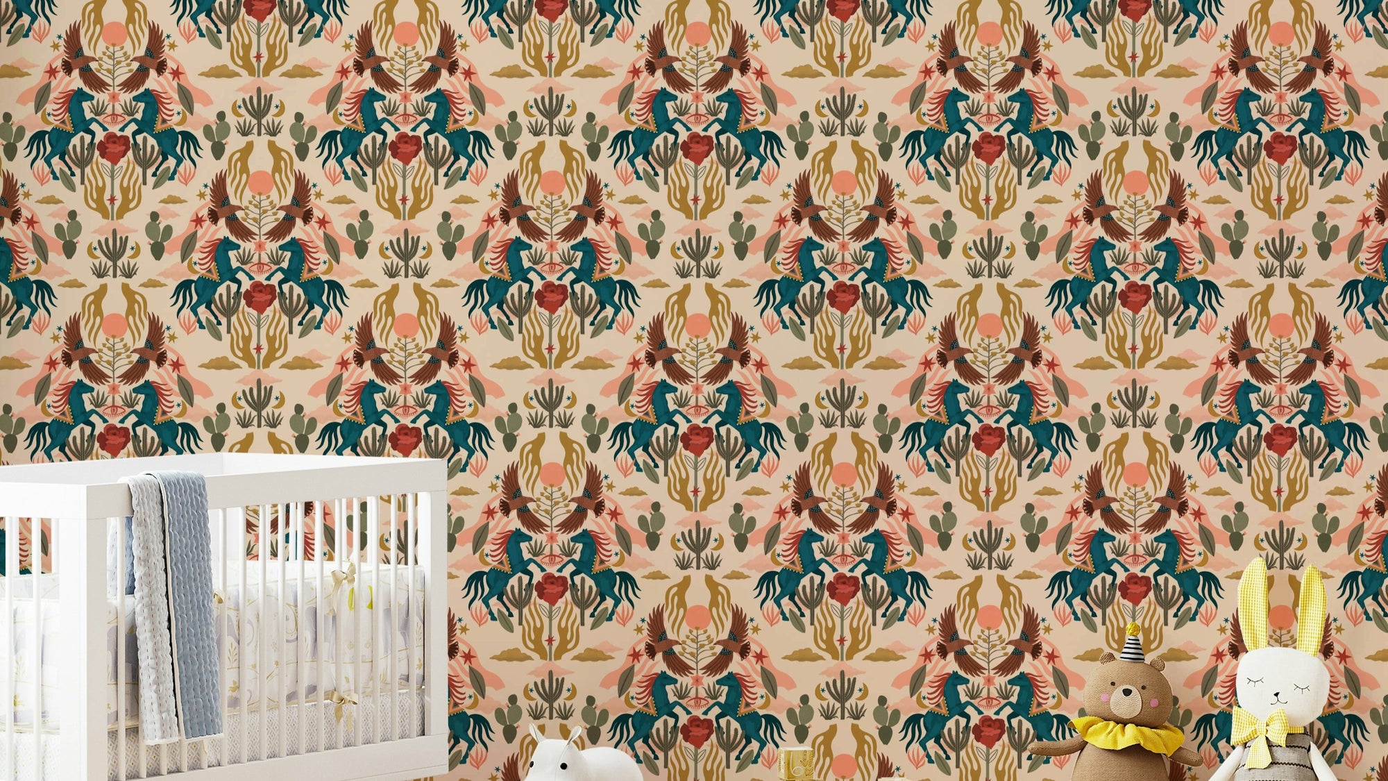 Wild West wallpaper with teal horses and cacti in a nursery with a white crib, grey blanket and plush toys